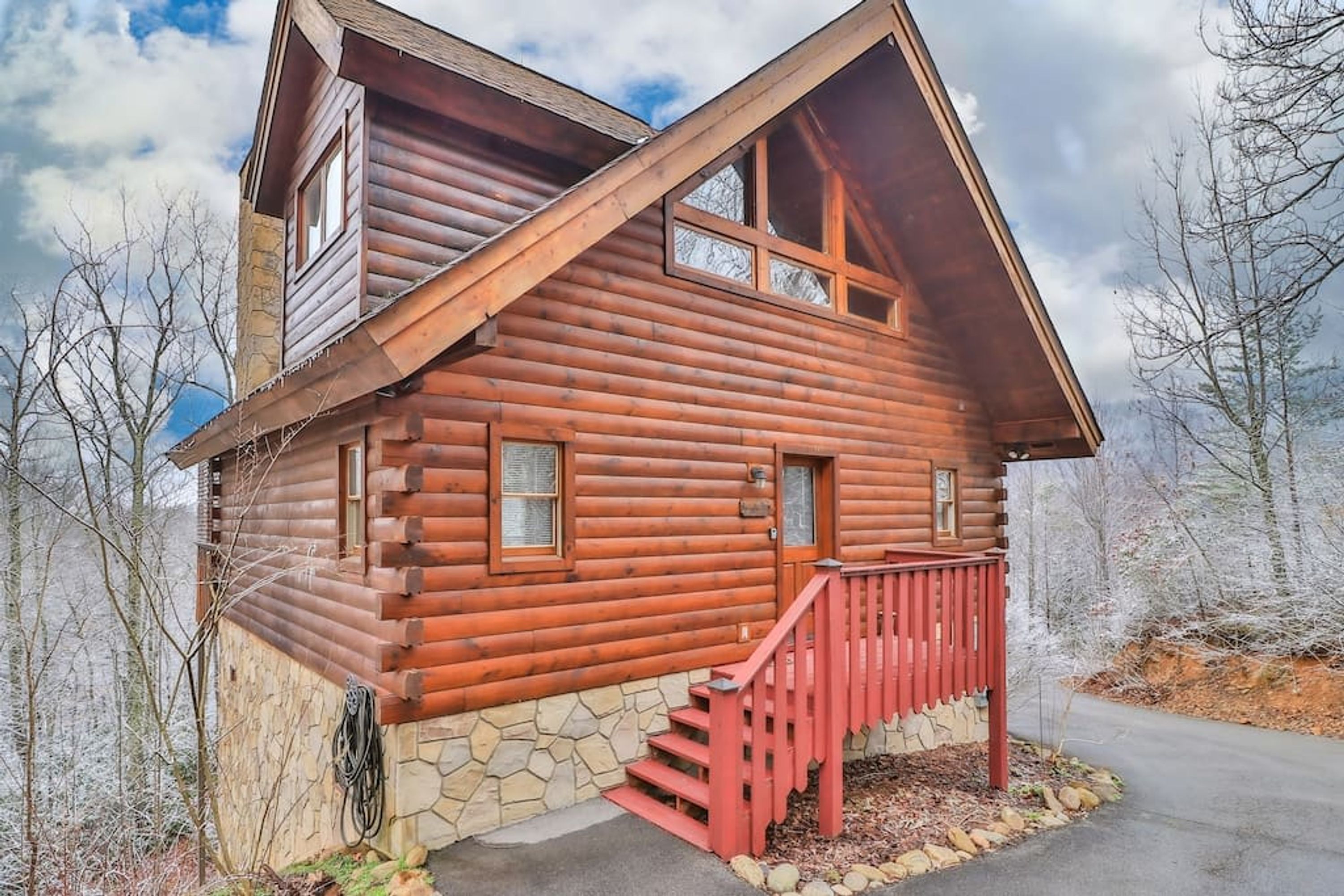 Eine Blockhütte mit Steinunterbau, einer roten Holztreppe und blauem Himmel.