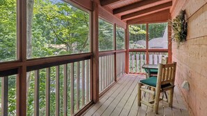 A covered porch with a table and chairs, large windows, and a view of trees. - Cabin Fever by Beyond Expectations With Hot Tub (Gatlinburg)