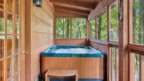 A wooden cabin with a hot tub, large windows, and a view of the forest. - Cabin Fever by Beyond Expectations With Hot Tub (Gatlinburg)