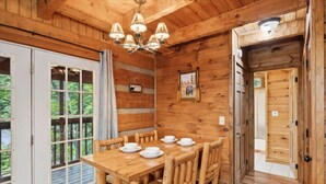 A wooden interior with a dining table set for four, a chandelier, and a door leading outside. - Cabin Fever by Beyond Expectations With Hot Tub (Gatlinburg)