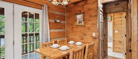 A wooden interior with a dining table set for four, a chandelier, and a door leading outside.