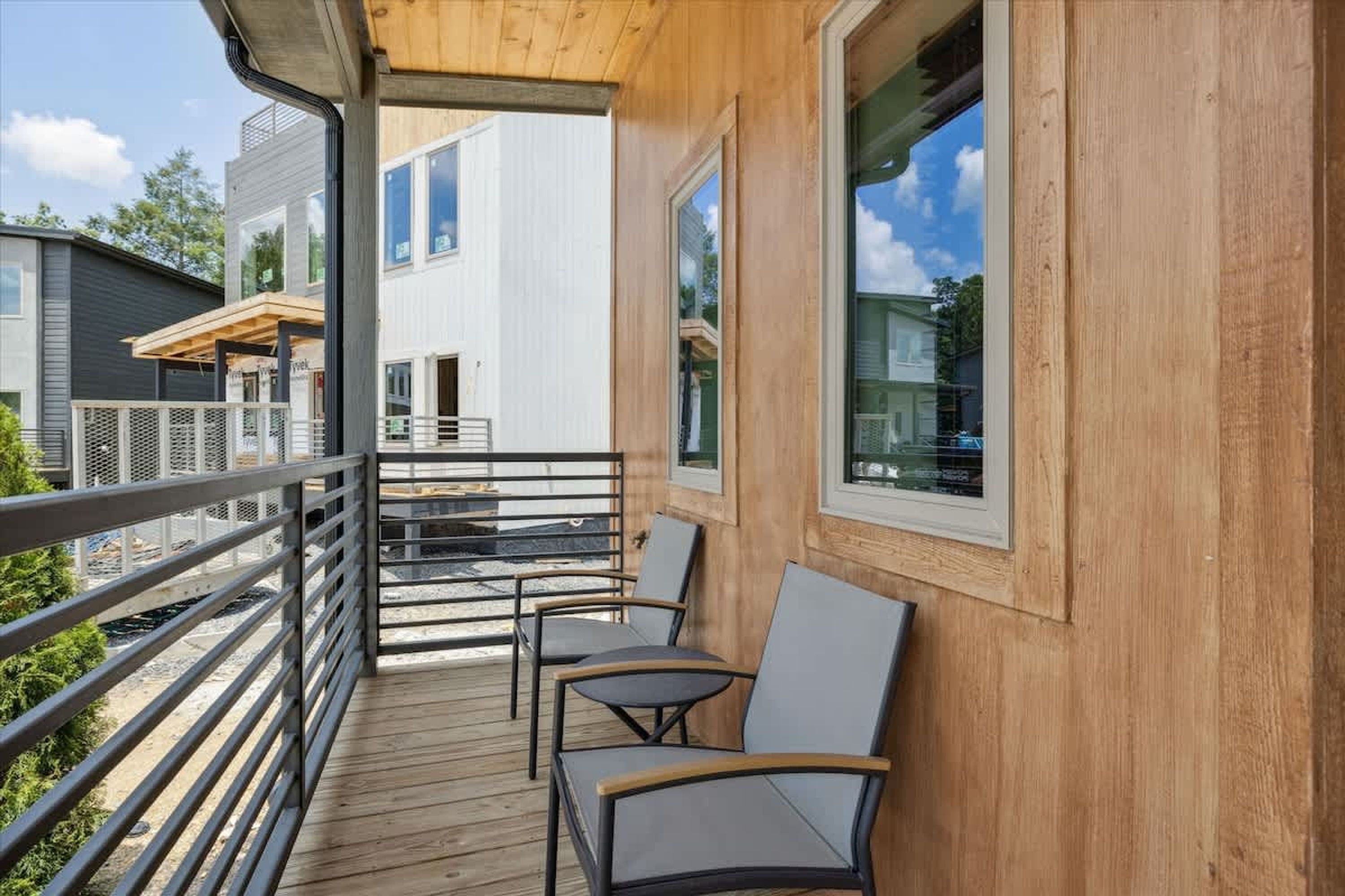 A wooden deck with chairs, a railing, and a view of a modern building.