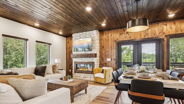 A cozy living room with a stone fireplace, wooden ceiling, and large windows. - Peak Pursuit by Beyond Expectations Mountain Home With Indoor Pool (Pigeon Forge)