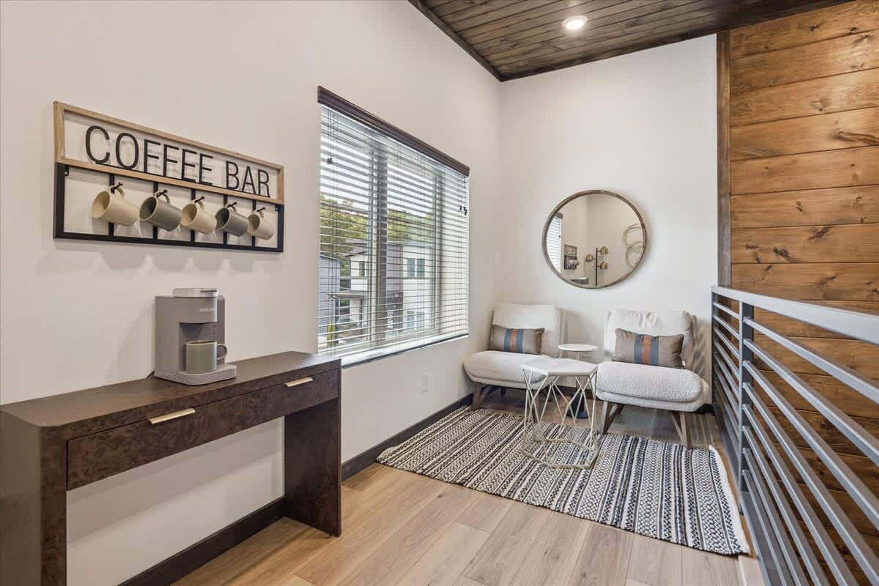 A modern room with a coffee bar, a round mirror, a sofa, and a view through a window.