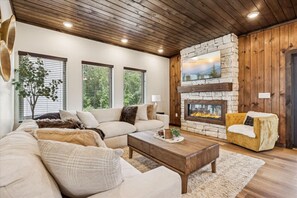 A living room with a stone fireplace, wooden ceiling, and a sofa. - Peak Pursuit by Beyond Expectations Mountain Home With Indoor Pool (Pigeon Forge)