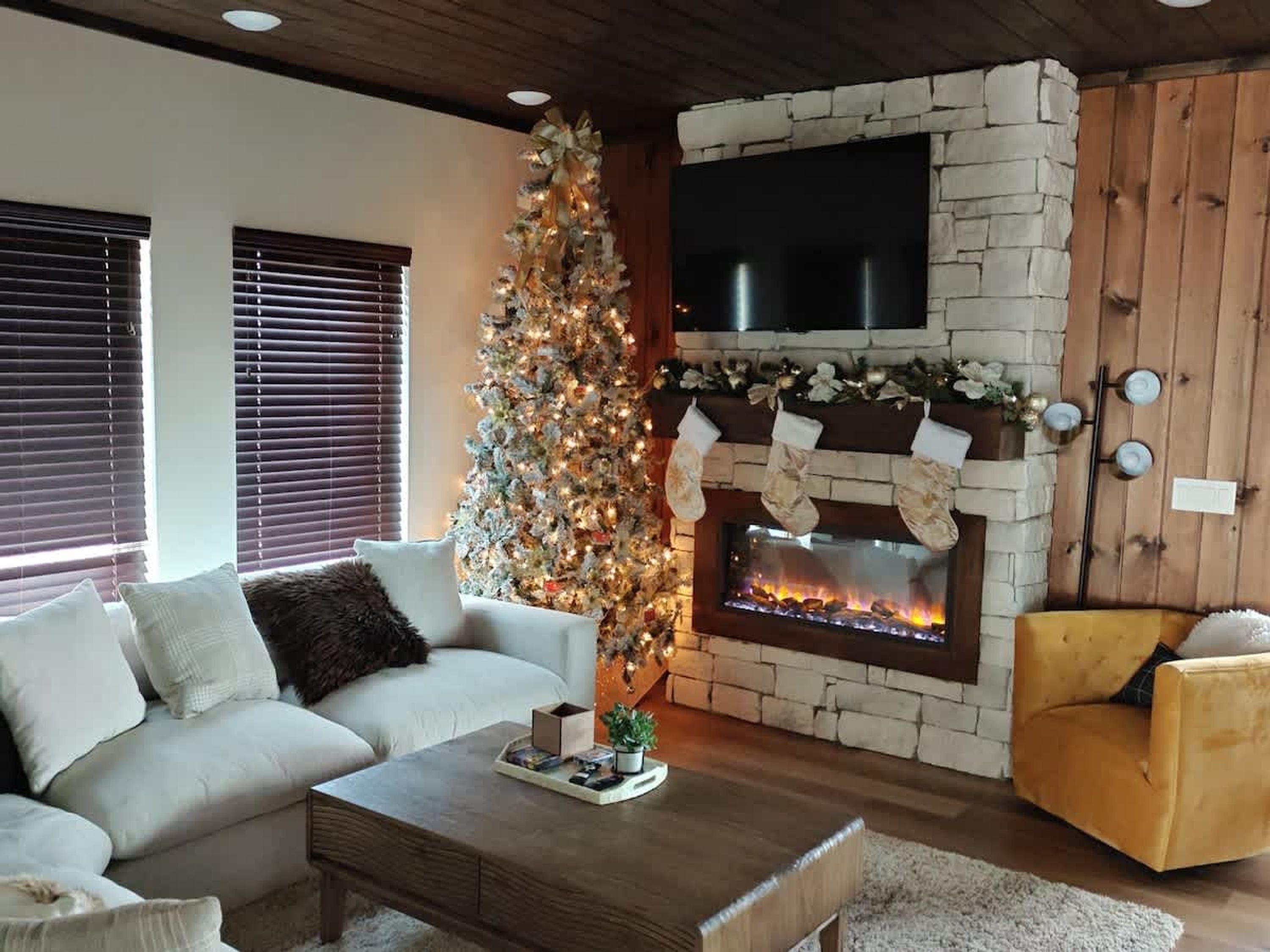 A cozy living room with a fireplace, a Christmas tree, a sofa, and a chair.