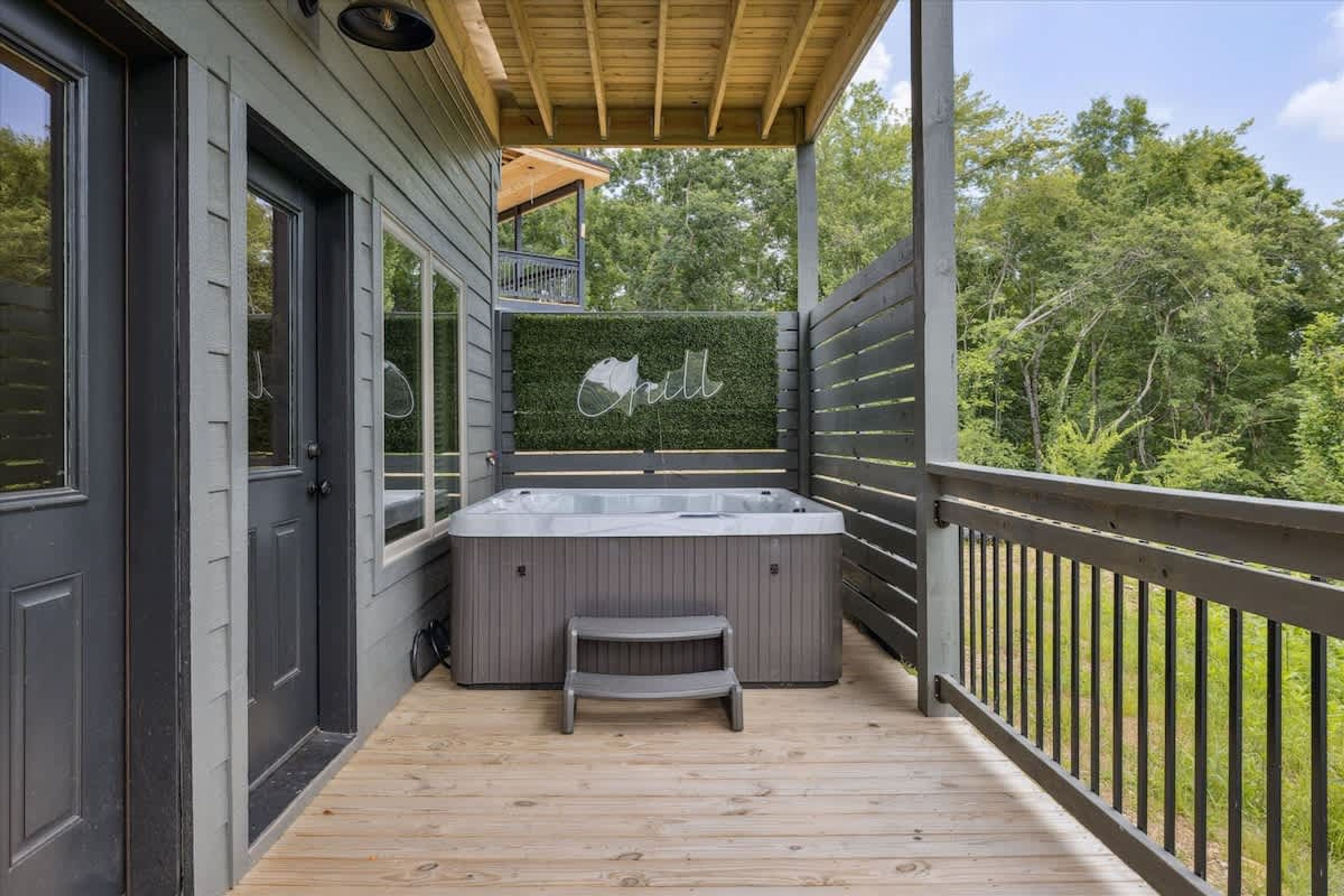 Eine Holzterrasse mit Whirlpool, einer kleinen Stufe und einer Wand mit einem Schild 'Grill'.