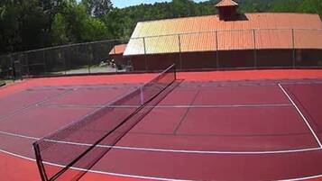 Een tennisbaan met een net, omringd door een hek en een gebouw met een rood dak.