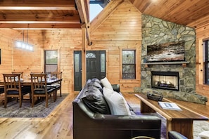 Interno di una baita in legno con camino in pietra, tavolo da pranzo in legno e una zona salotto accogliente.