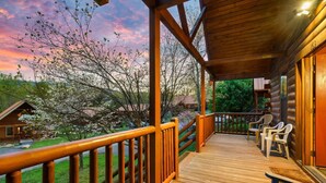 A wooden deck with chairs, a railing, and a view of a house and trees. - Dotties Place Cabin by Beyond Expectations With Hot Tub (Gatlinburg)