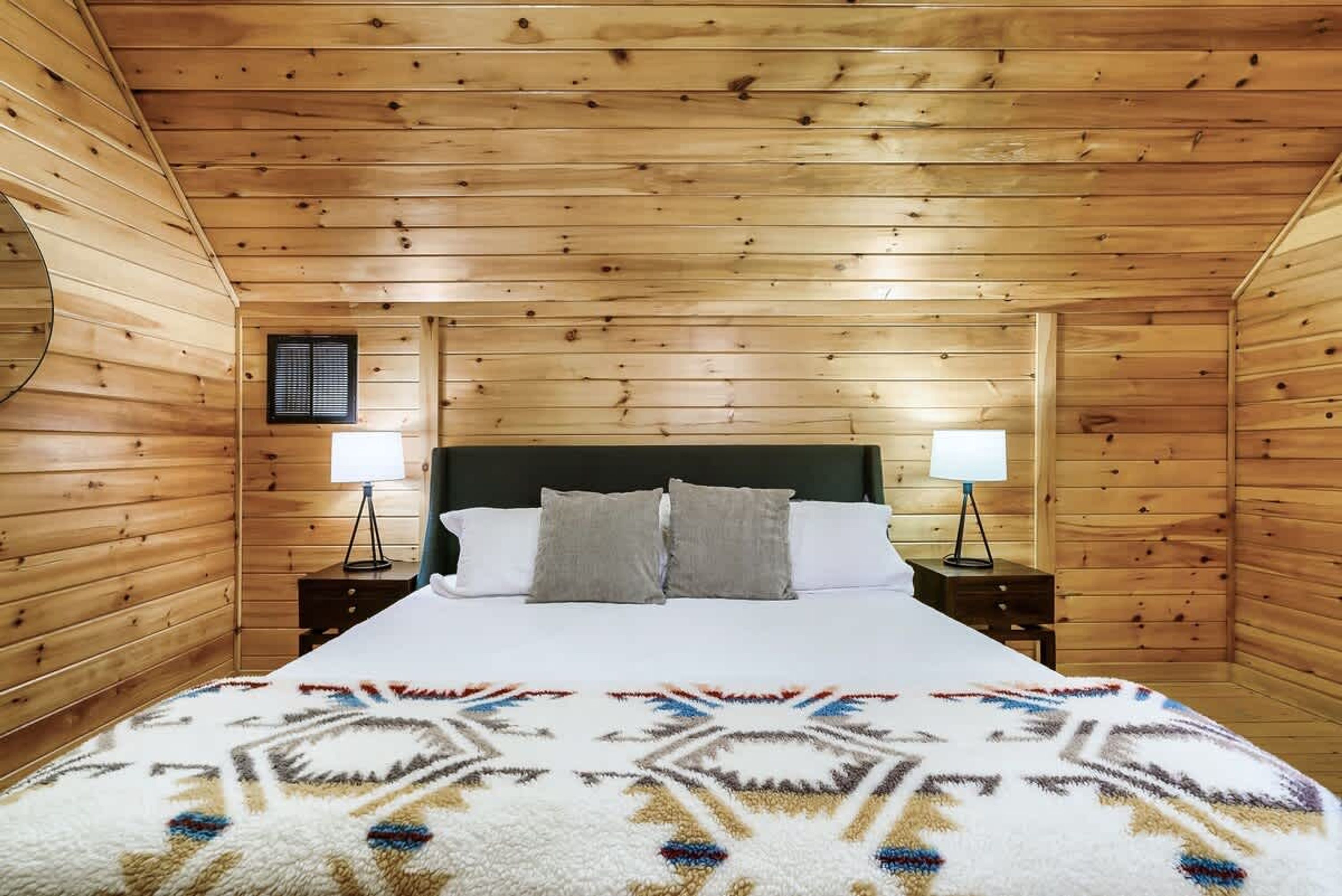 A wooden-paneled room with a bed, two bedside tables, and a window.