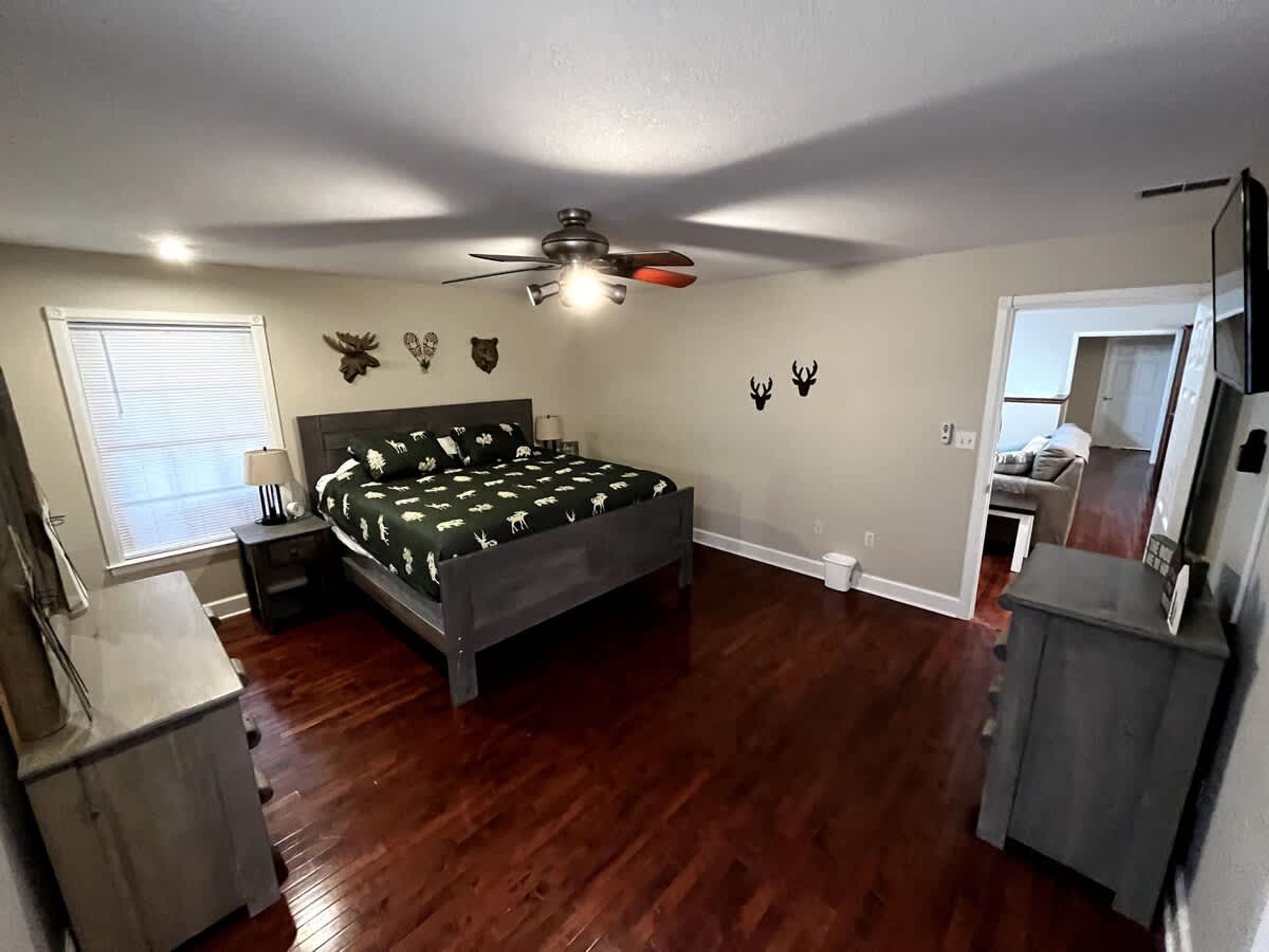 A bedroom with a bed, a ceiling fan, a window with blinds, and a small bathroom.