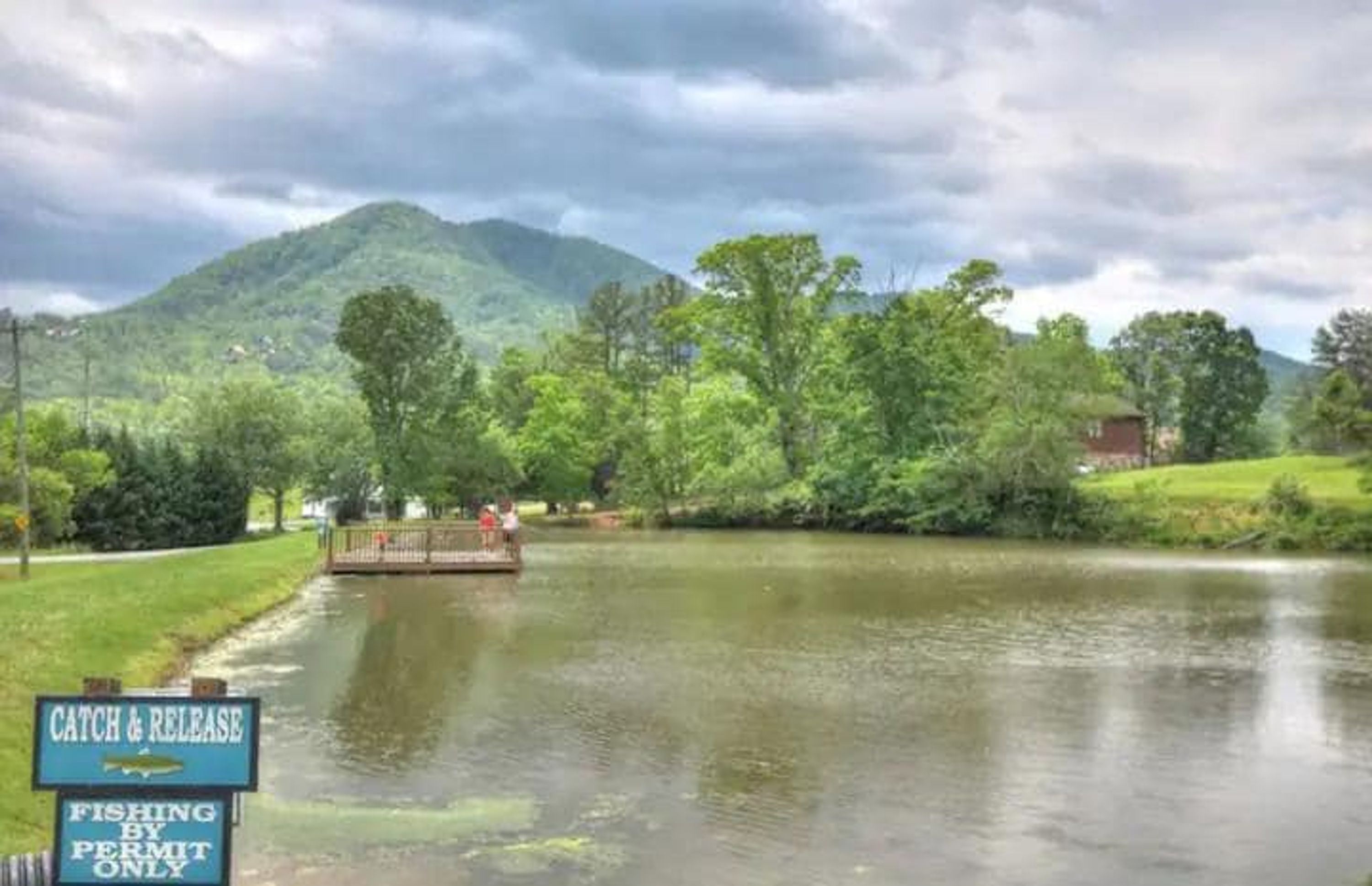 Um lago com uma ponte, rodeado por vegetação e montanhas.