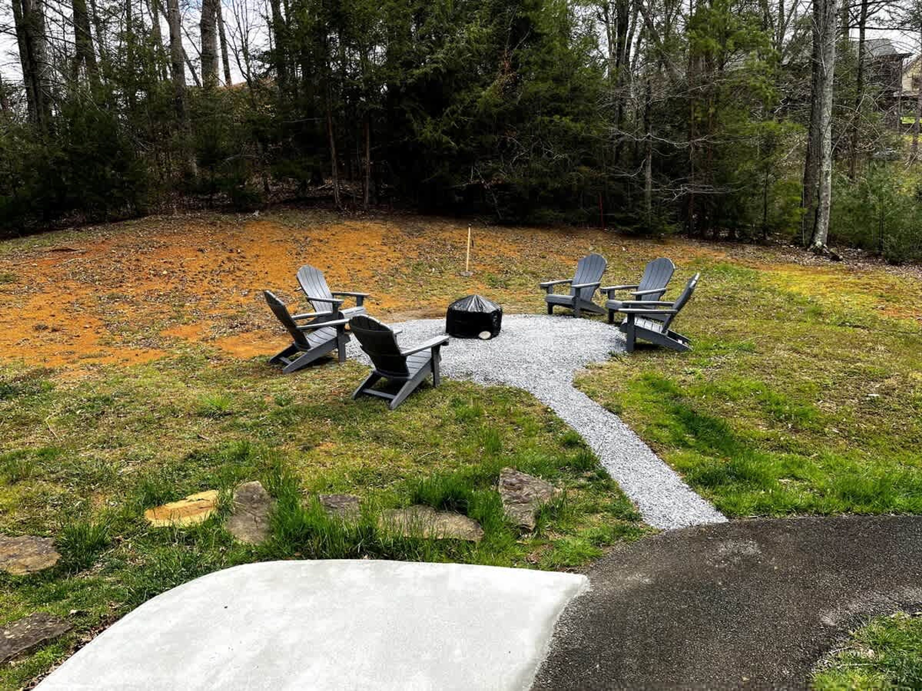 A gravel patio with four Adirondack chairs and a fire pit.
