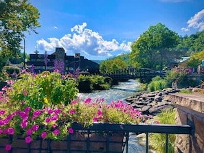 Une rivière traversée par un pont, une végétation luxuriante et, au loin, un bâtiment surmonté d’une tour.