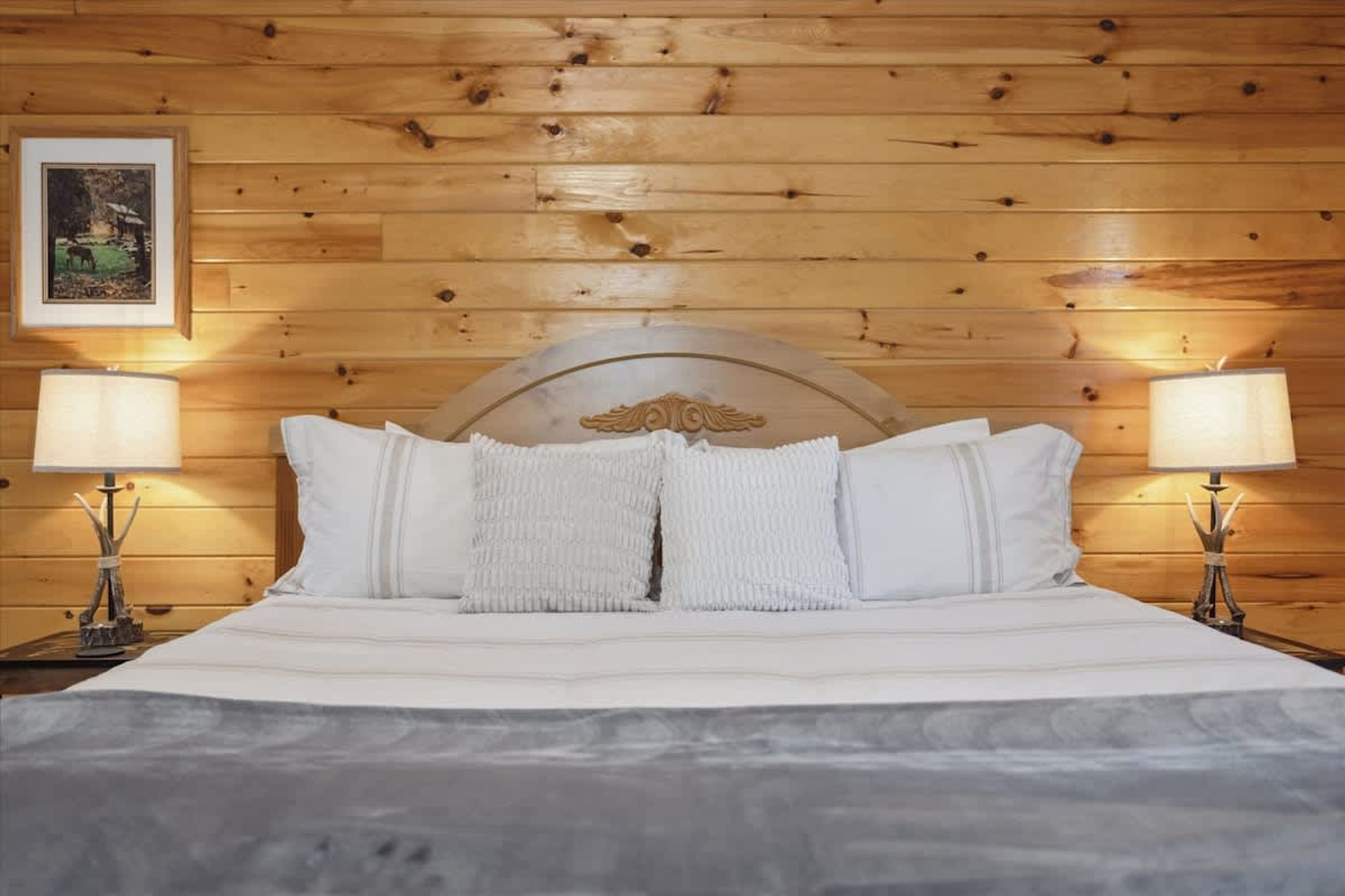 A wooden-paneled room with a bed, two bedside lamps, and a framed picture on the wall.