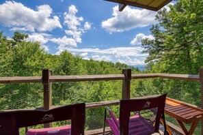 A wooden deck with chairs and a table, overlooking a forested area. - 1023 English Mtn Condo By Beyond Expectations (Sevierville)