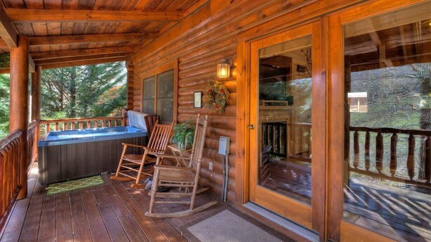 A wooden cabin with a covered porch, a hot tub, rocking chairs, and a fireplace. - Snuggle Up Cabin by Beyond Expectations With Hot Tub (Sevierville)