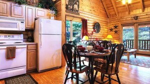 A wooden cabin interior with a kitchen, dining area, and large windows. - Snuggle Up Cabin by Beyond Expectations With Hot Tub (Sevierville)