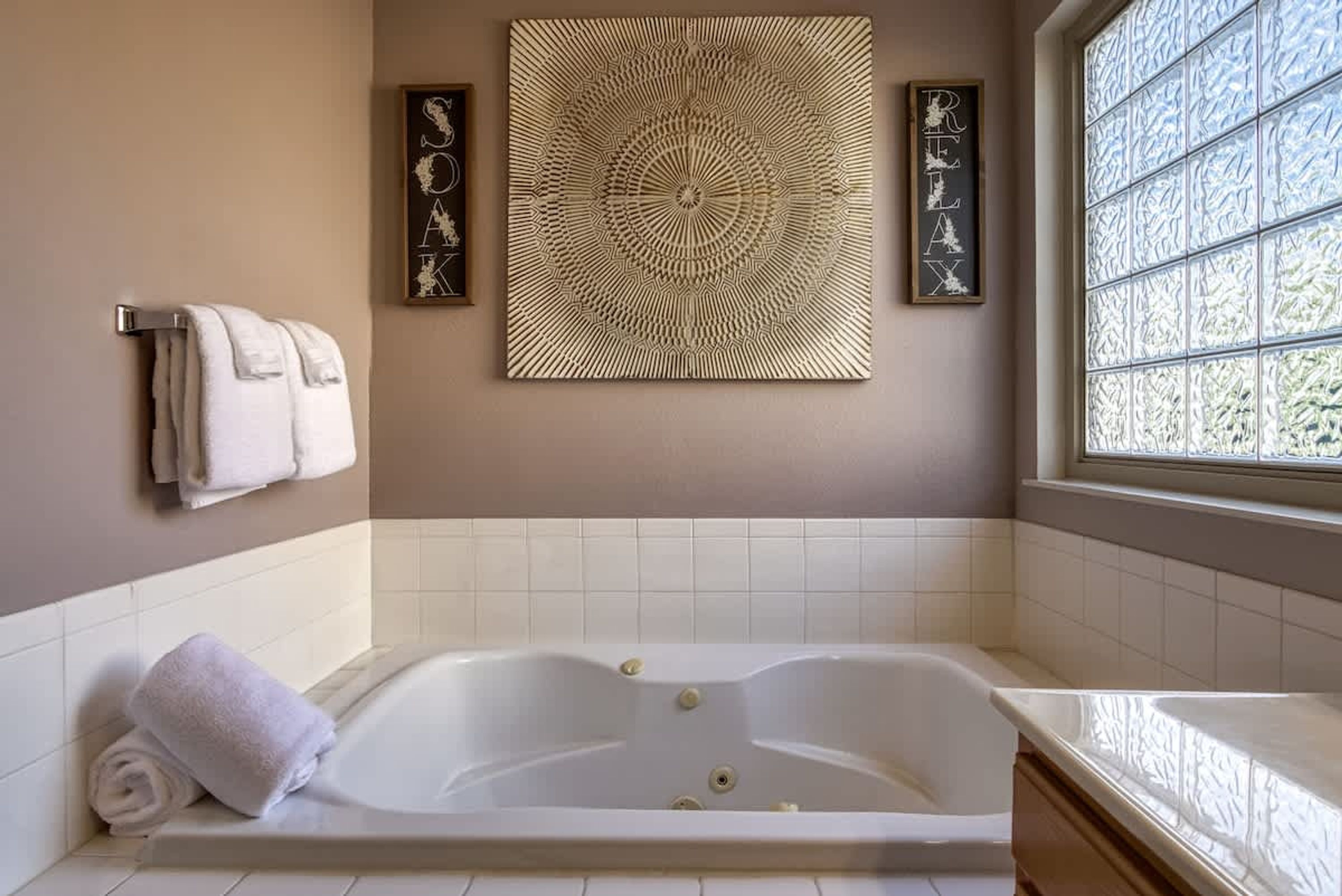 A bathroom with a large bathtub, a towel rack, and a decorative wall piece.