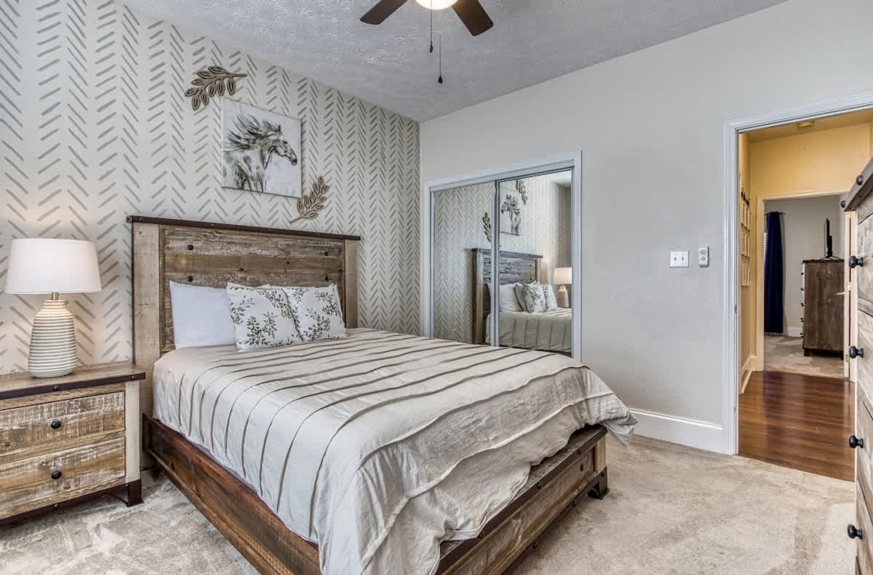 A bedroom with a bed, nightstand, lamp, and a mirror.
