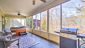 Un patio cubierto con un jacuzzi, mobiliario exterior, una parrilla y amplias ventanas con vistas a árboles.
