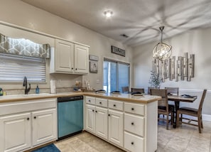 A kitchen with white cabinetry, a dishwasher, a dining area with a wooden table and chairs, and a wall-mounted light fixture. - Saddleback Retreat by Beyond Expectations (Sevierville)