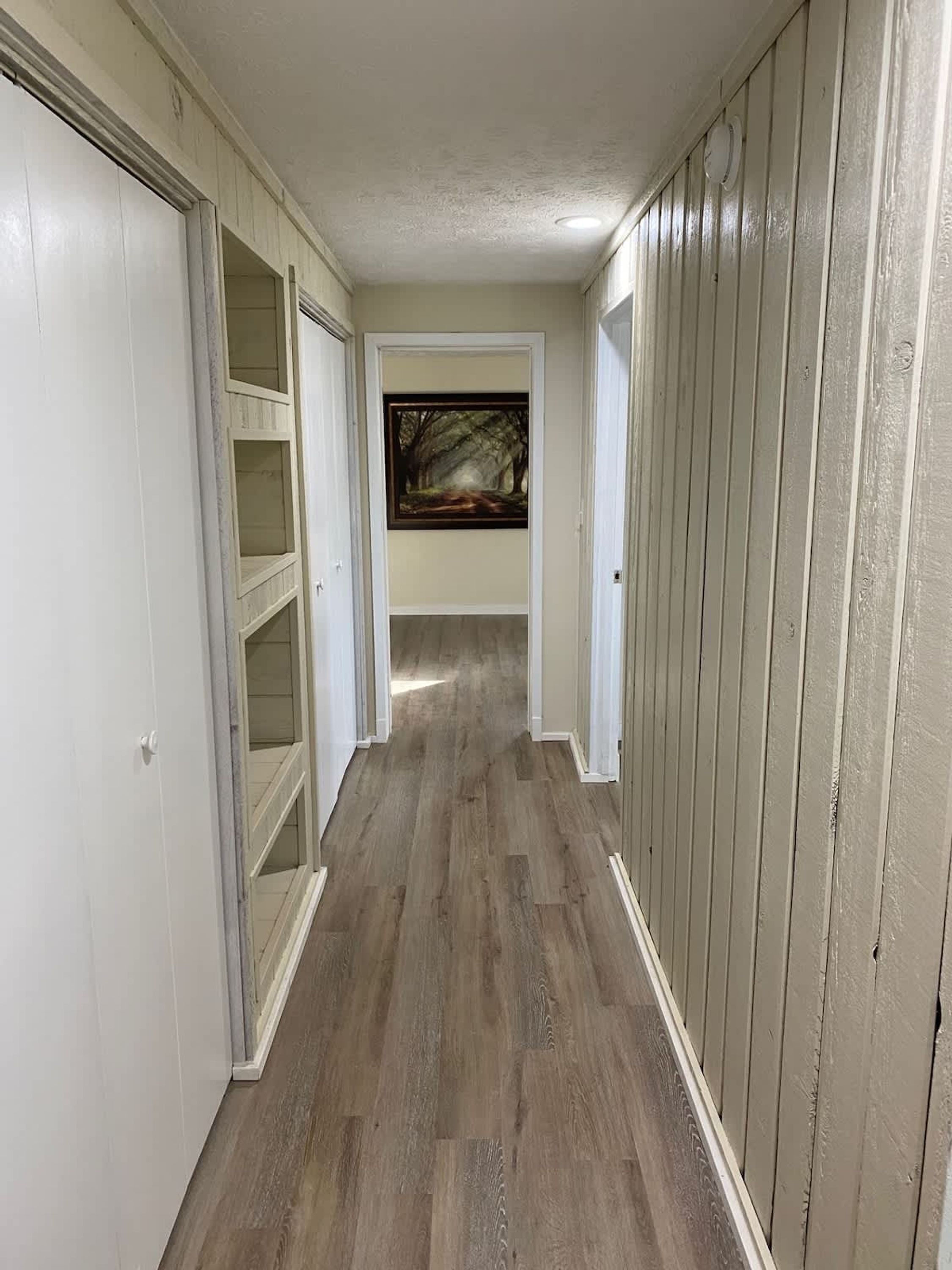 Un pasillo con piso de madera, paredes blancas y un cuadro en la pared.