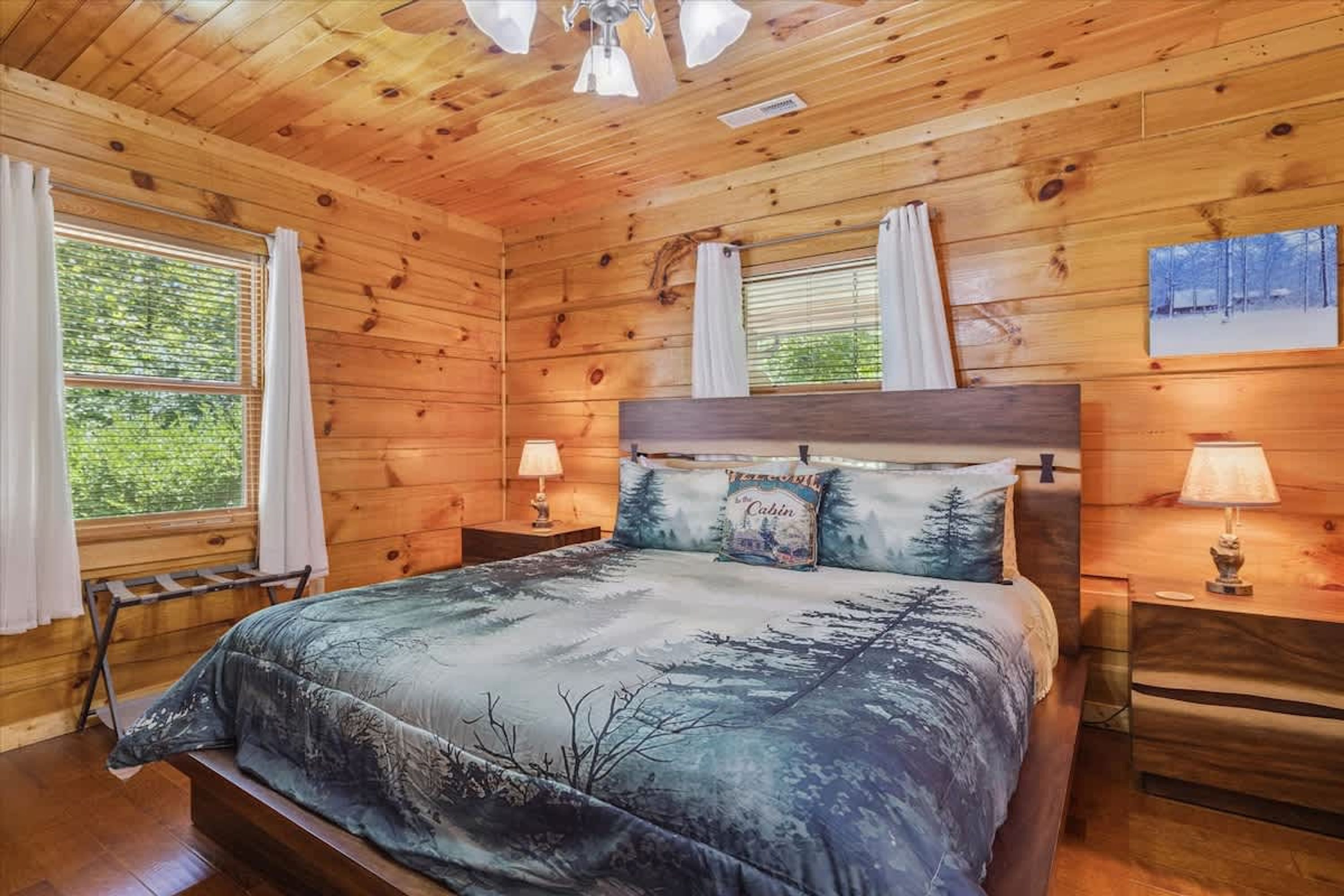 A wooden cabin bedroom with a bed, two bedside tables, and a window with curtains.