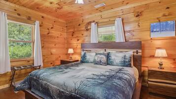 A wooden cabin bedroom with a bed, two bedside tables, and a window with curtains.