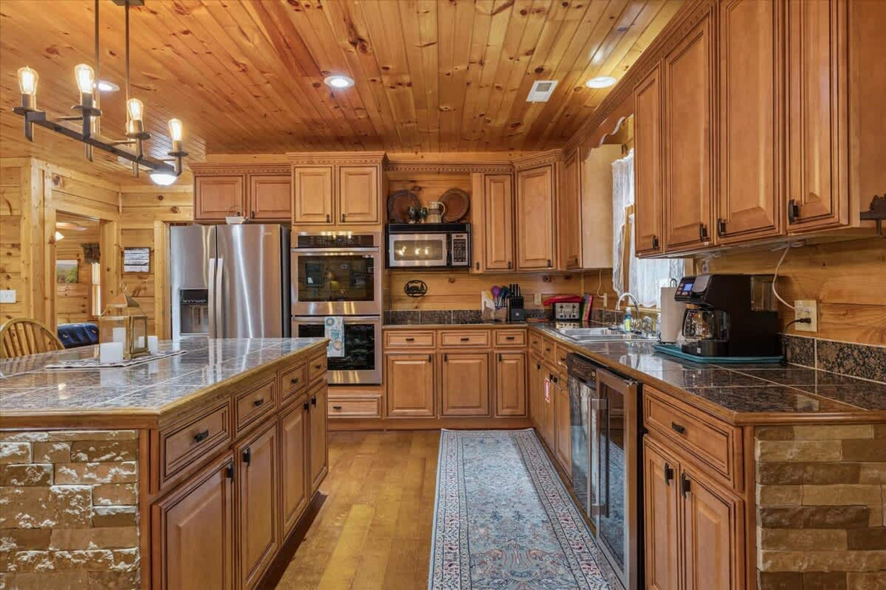Interior de una cabaña de madera con cocina que cuenta con encimeras de granito, electrodomésticos de acero inoxidable y armarios de madera.
