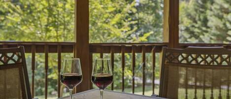 A table with two wine glasses on a balcony with a view of trees.