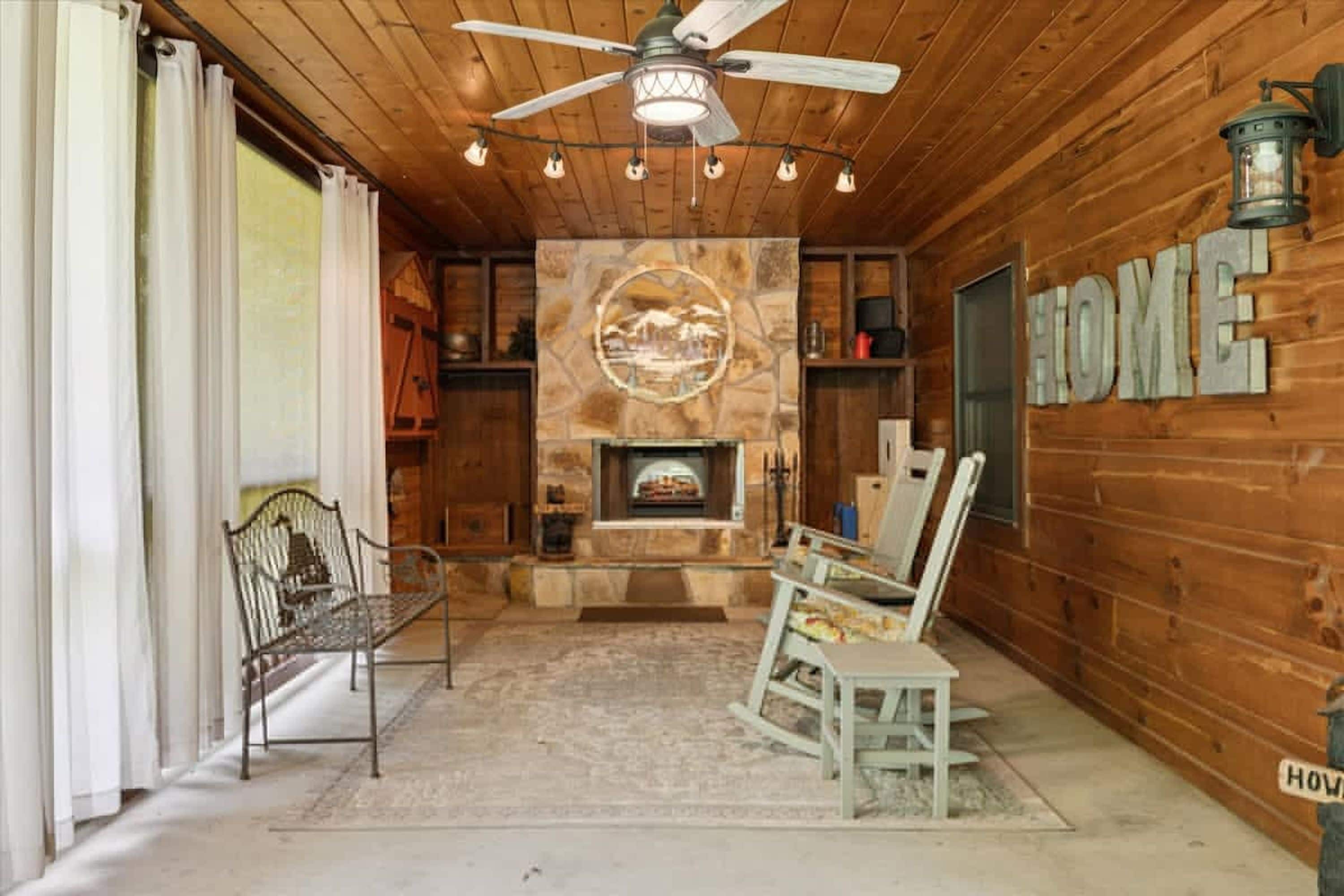 A cozy interior with a stone fireplace, wooden walls, a ceiling fan, and a bench.