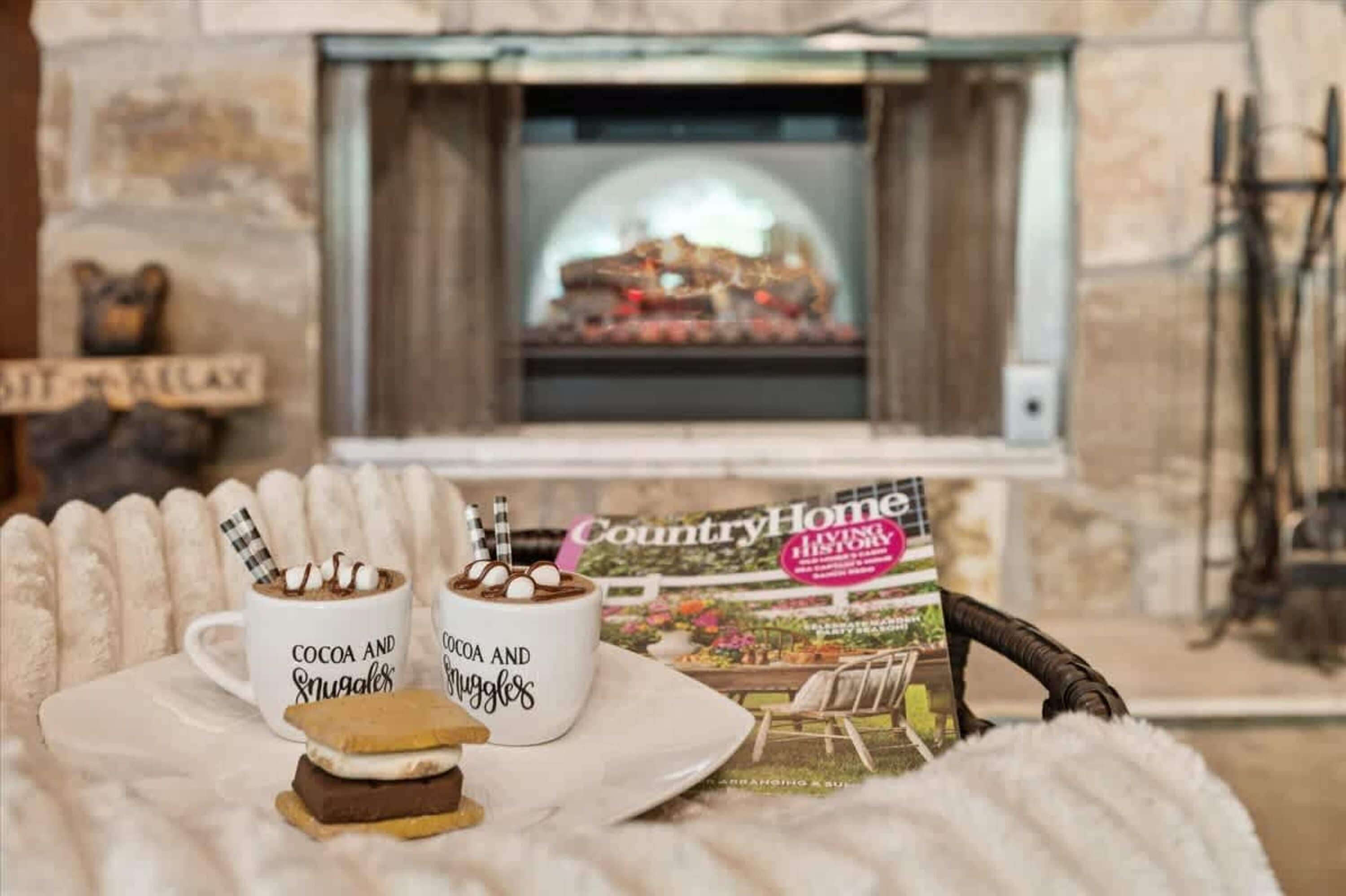 Una habitación acogedora con chimenea, dos tazas que dicen 'Cocoa' y 'Snugglers', y una revista titulada 'CountryHome'.