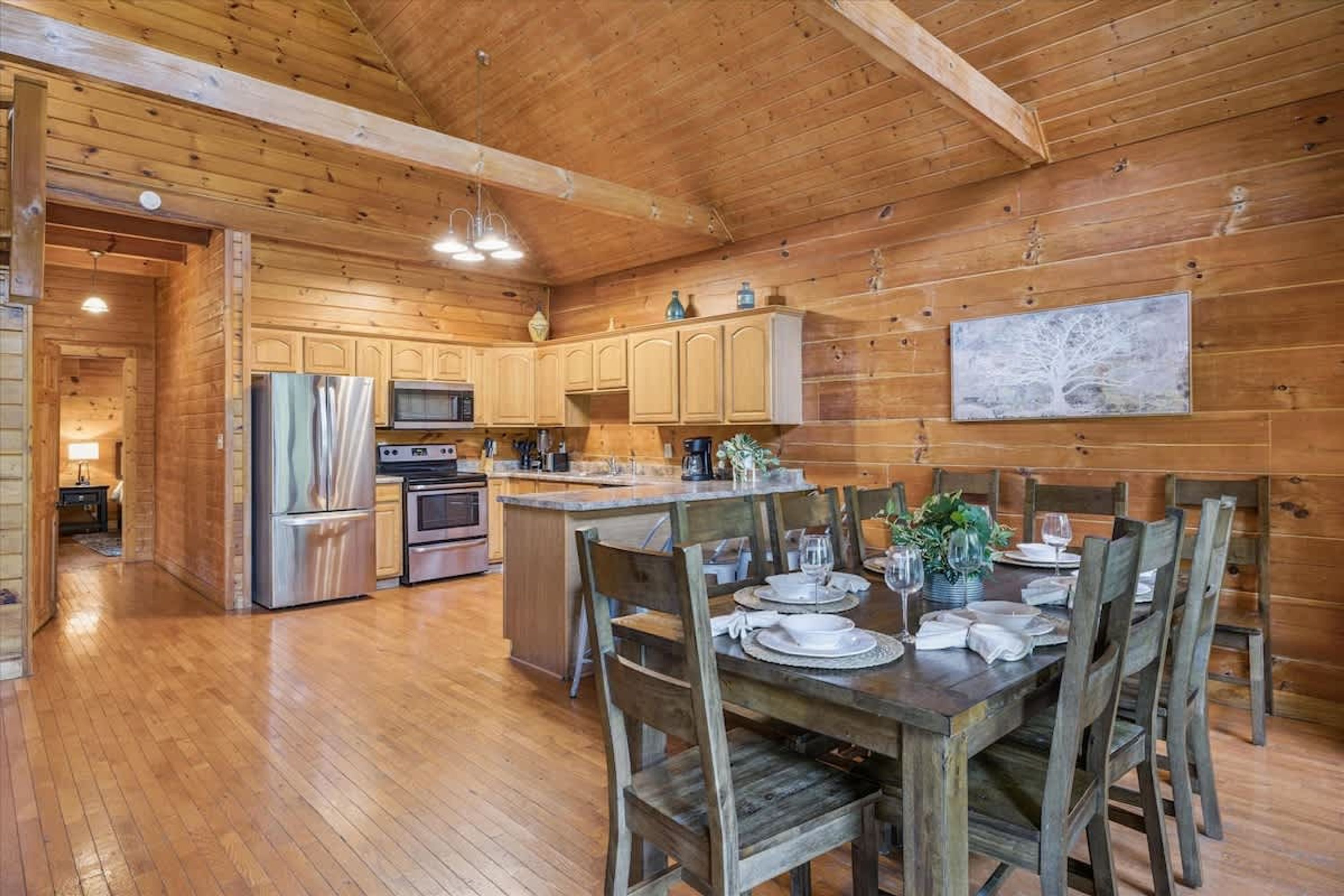 A wooden cabin interior with a kitchen, dining area, and a large wooden-framed ceiling.