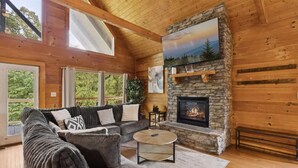 Ein gemütliches Blockhaus-Interieur mit Kamin aus Stein, einer großen Couch und einer Holzbalkendecke.