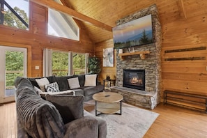 A cozy cabin interior with a stone fireplace, a large sofa, and a wooden ceiling. - Beauty By The River Lodge by Beyond Expectations (Sevierville)