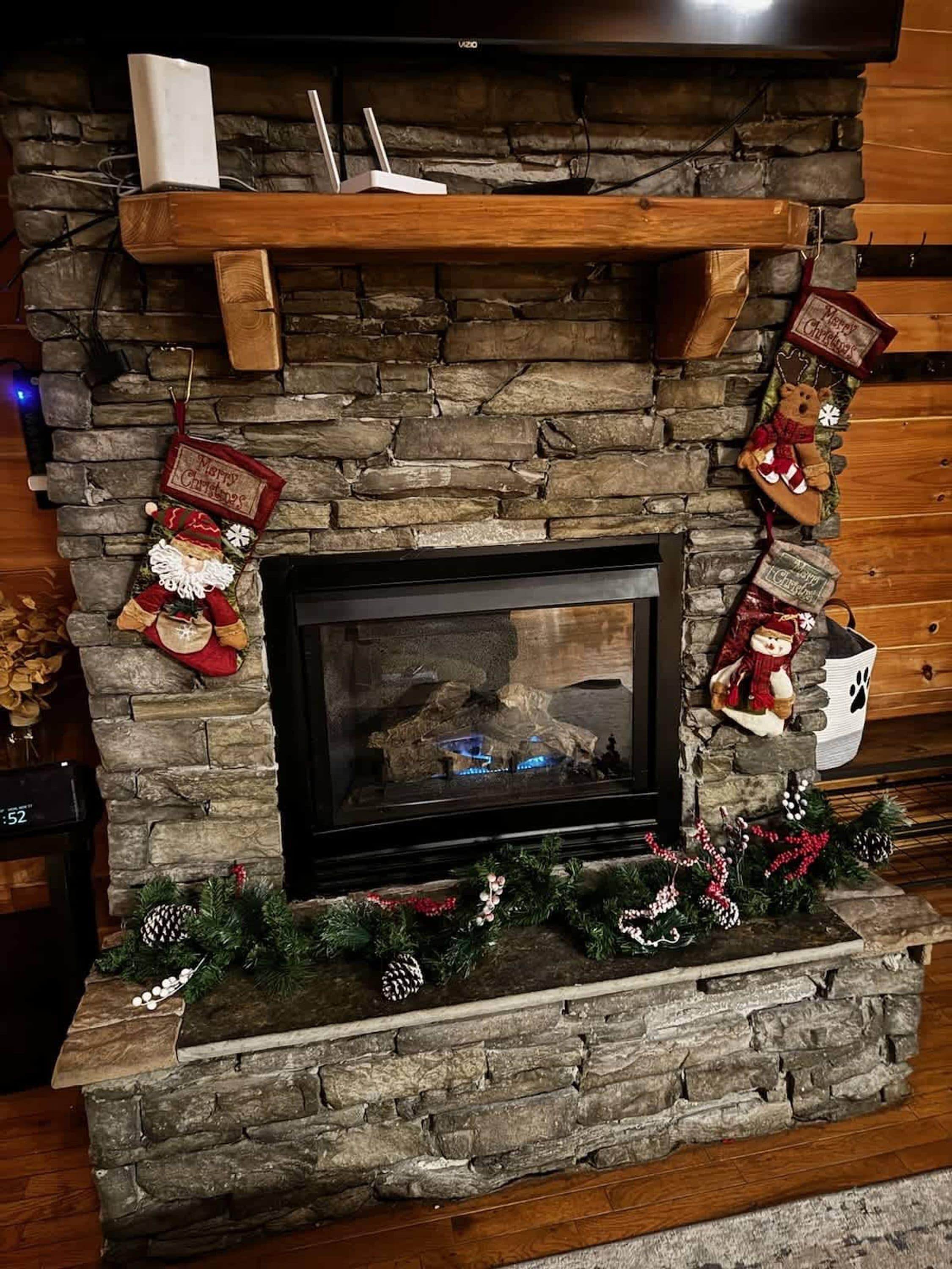 A stone fireplace with a black screen, surrounded by Christmas decorations including stockings and garlands.