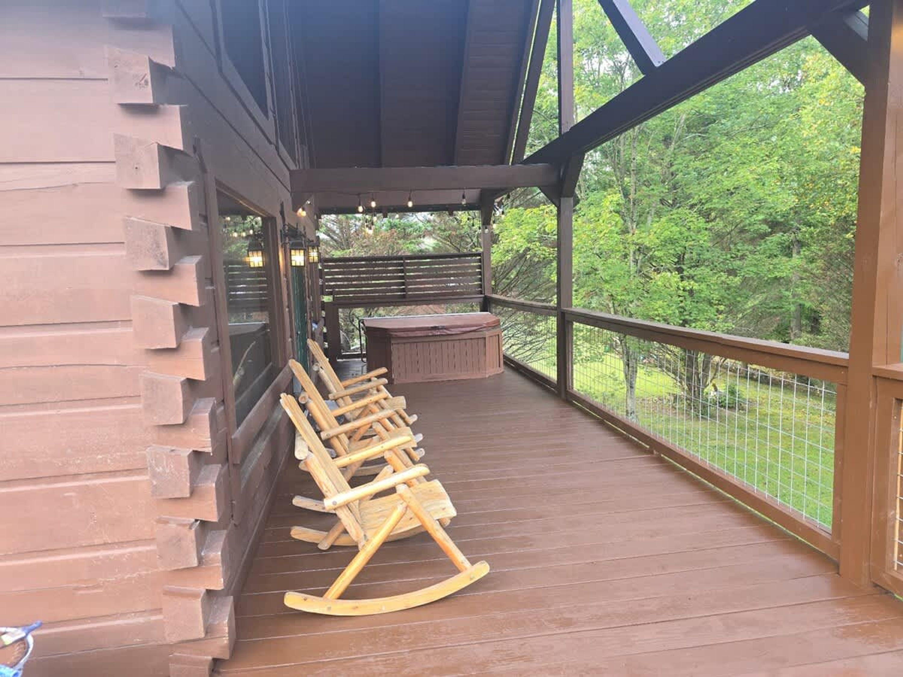Um deck de madeira com cadeiras de balanço e um banco, com vista para um jardim cercado.