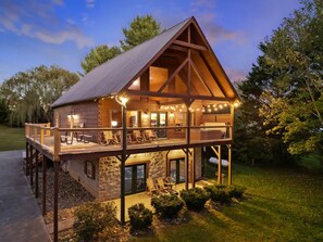 Une cabane en bois dotée d’un balcon, de fondations en pierre et illuminée de guirlandes lumineuses.