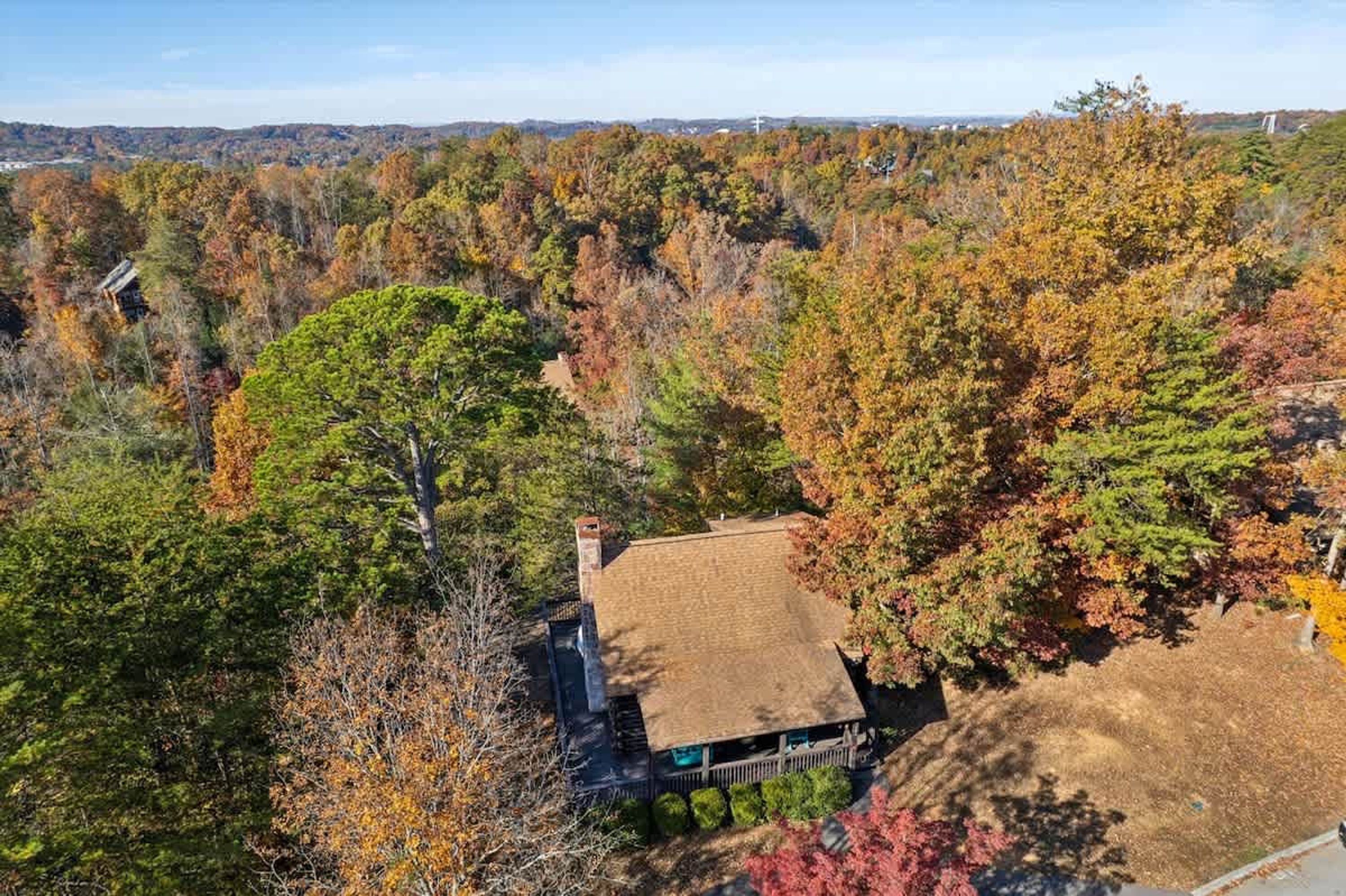 A house surrounded by autumn foliage, with a visible chimney and a clear view of the surrounding forest.
