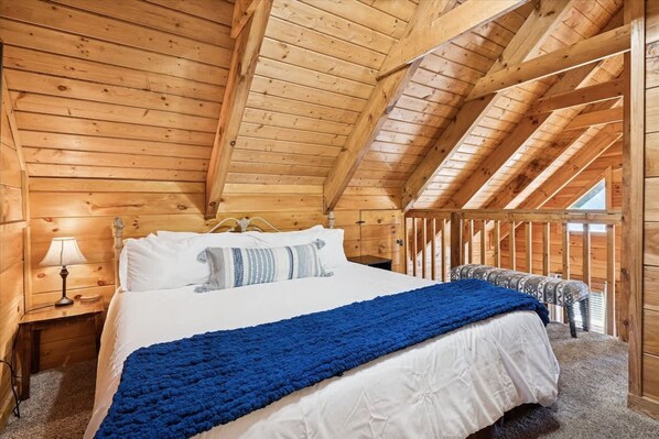 A wooden cabin bedroom with a bed, a nightstand, and a window. - Firefly Holler Cabin by Beyond Expectations With Hot Tub (Pigeon Forge)