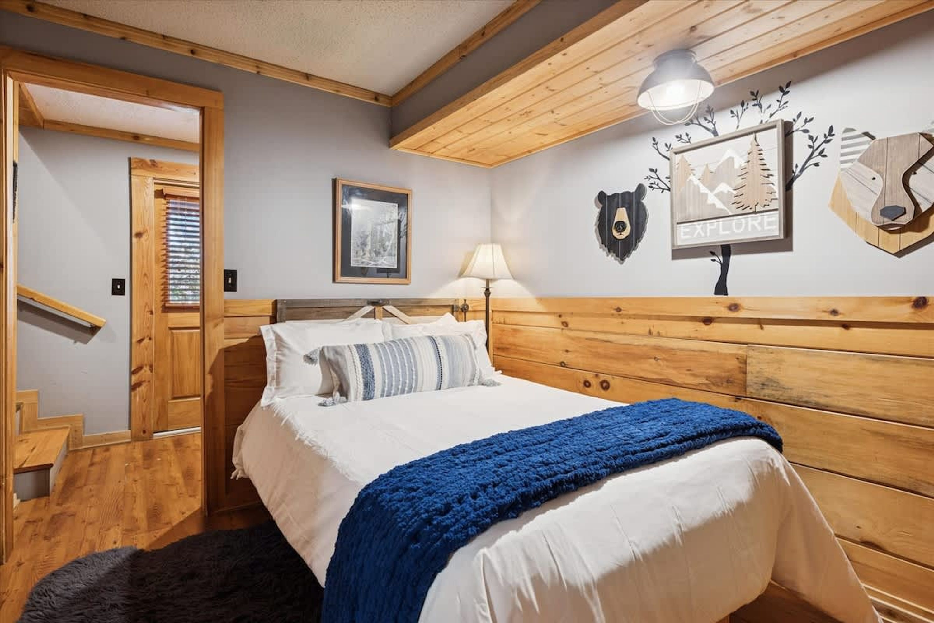 A bedroom with a wooden headboard, a bed with white bedding and a blue blanket, a framed picture on the wall, and a sign that says 'EXPLORE'.