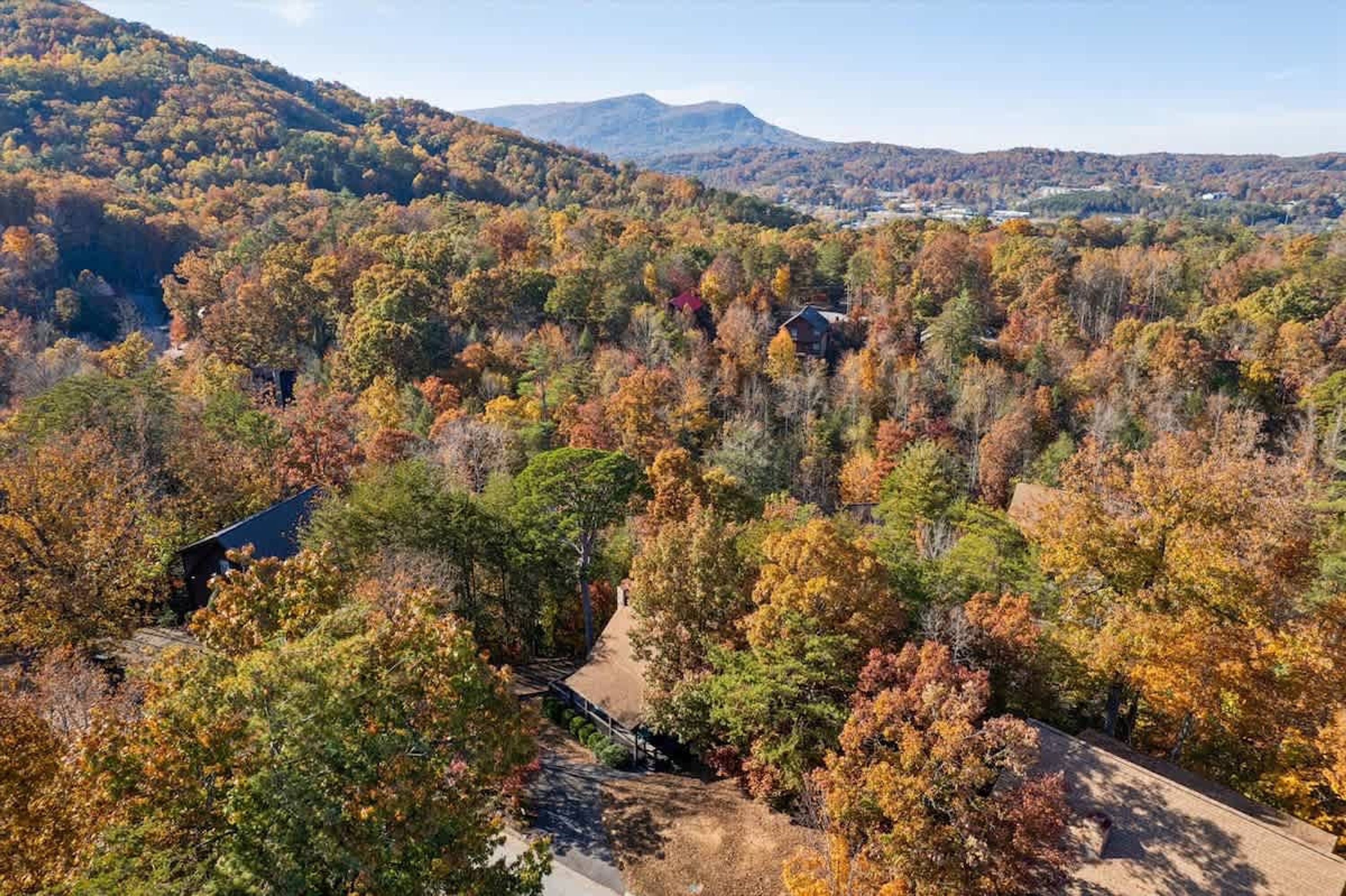 A mountainous landscape with autumn foliage, a cabin, and a clear sky.