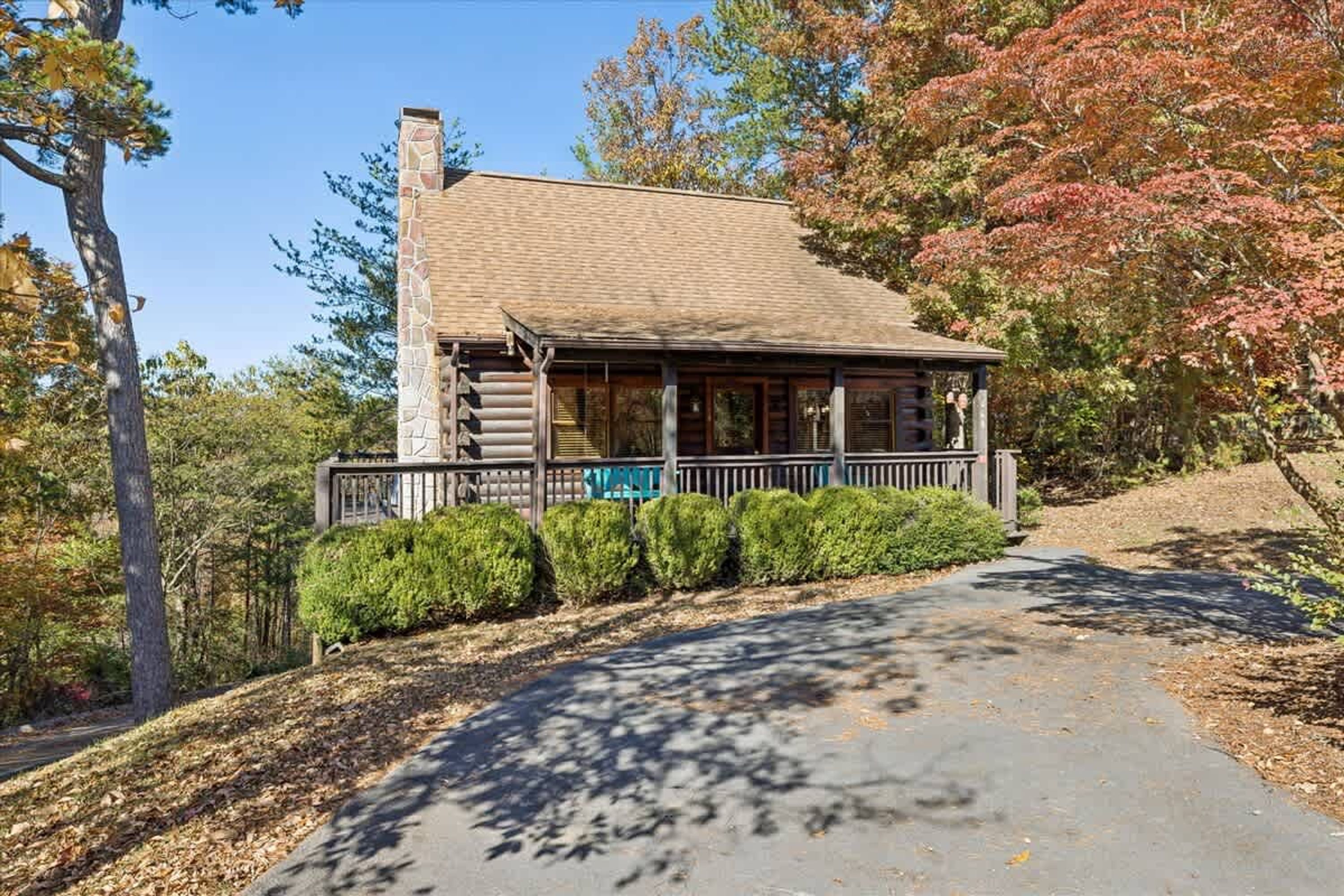 A log cabin with a porch, surrounded by trees and a pathway.