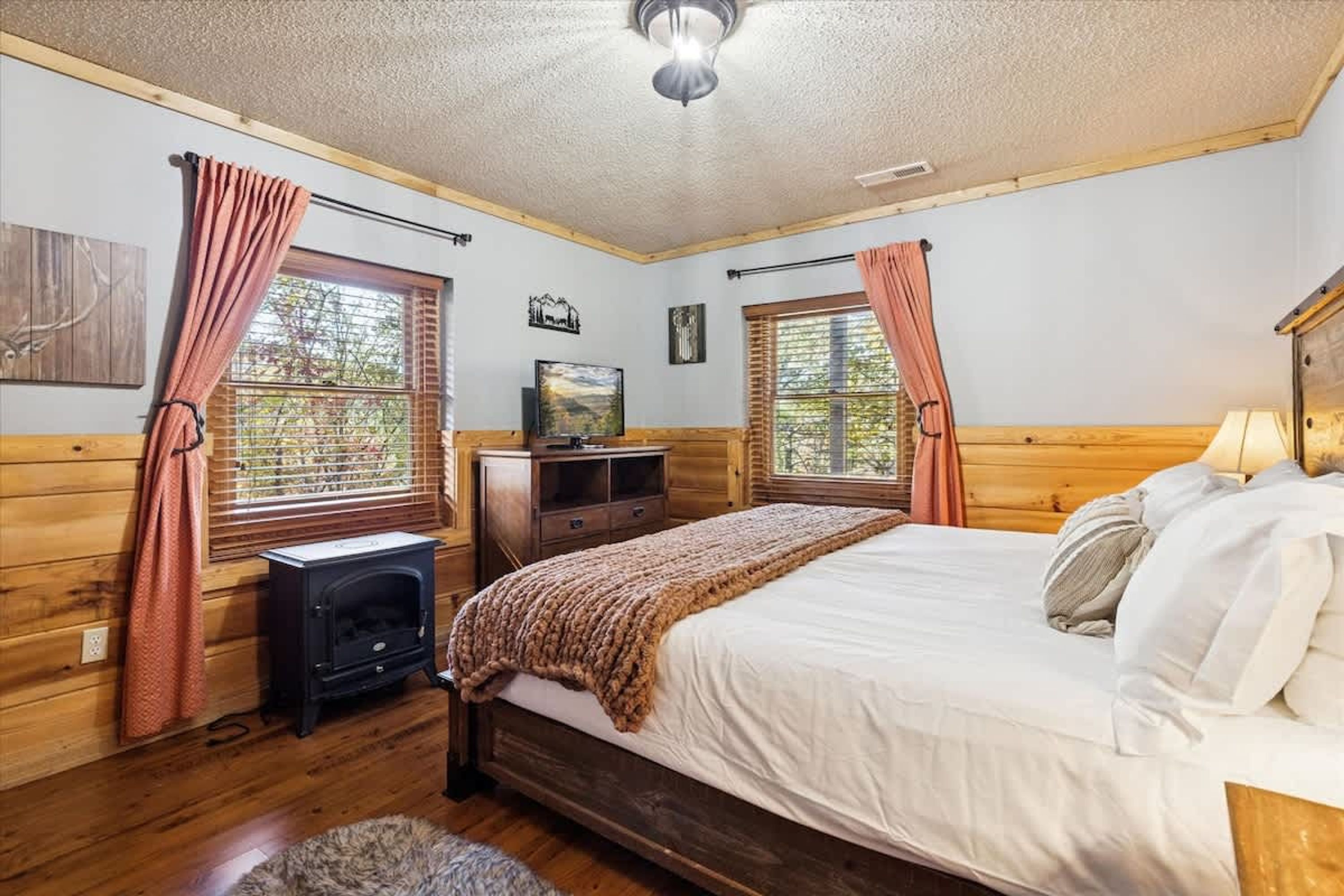Un dormitorio con cama, televisor, chimenea y ventanas con cortinas.