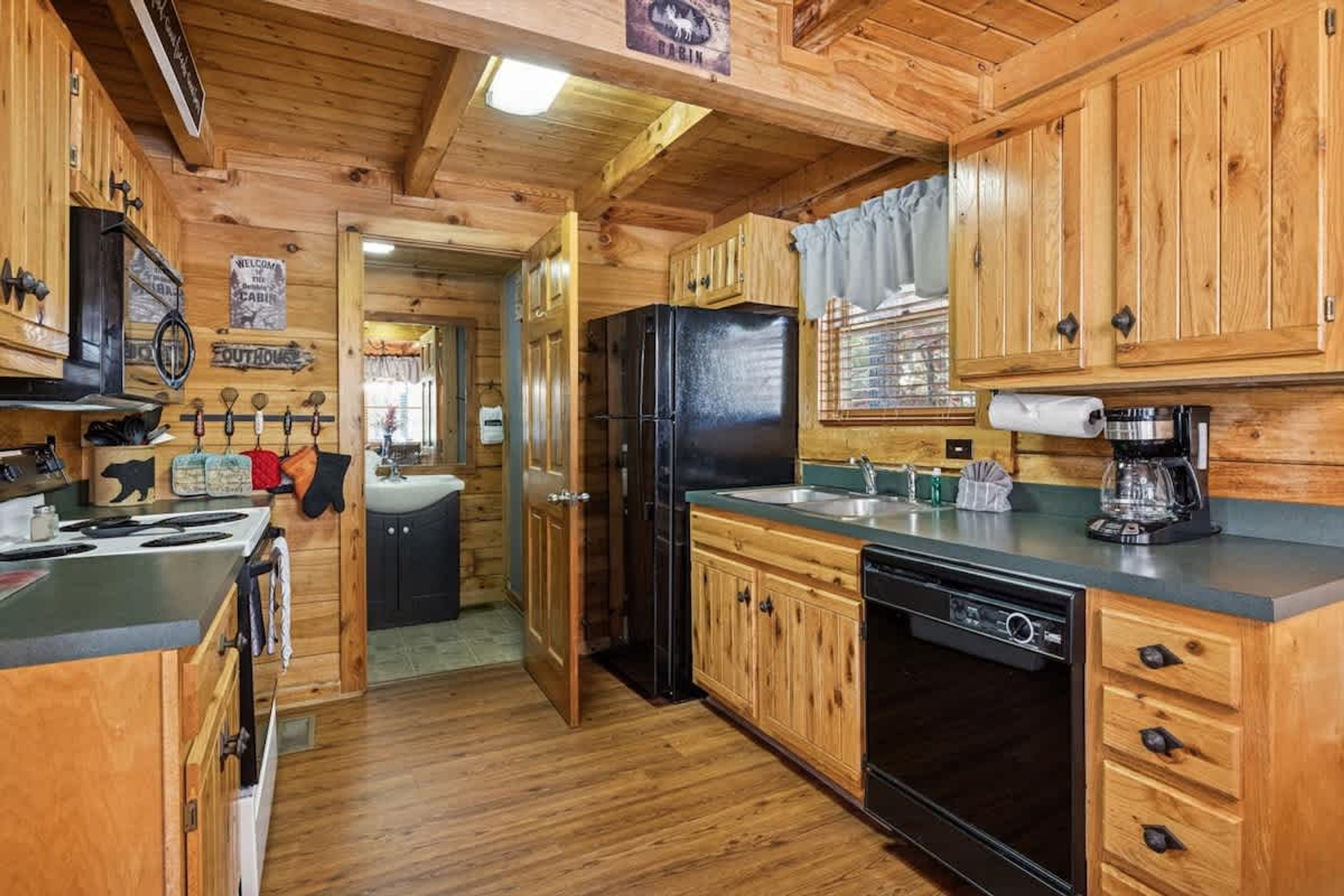 A cabin-style kitchen with wooden cabinets, a black refrigerator, a stove, and a coffee maker.