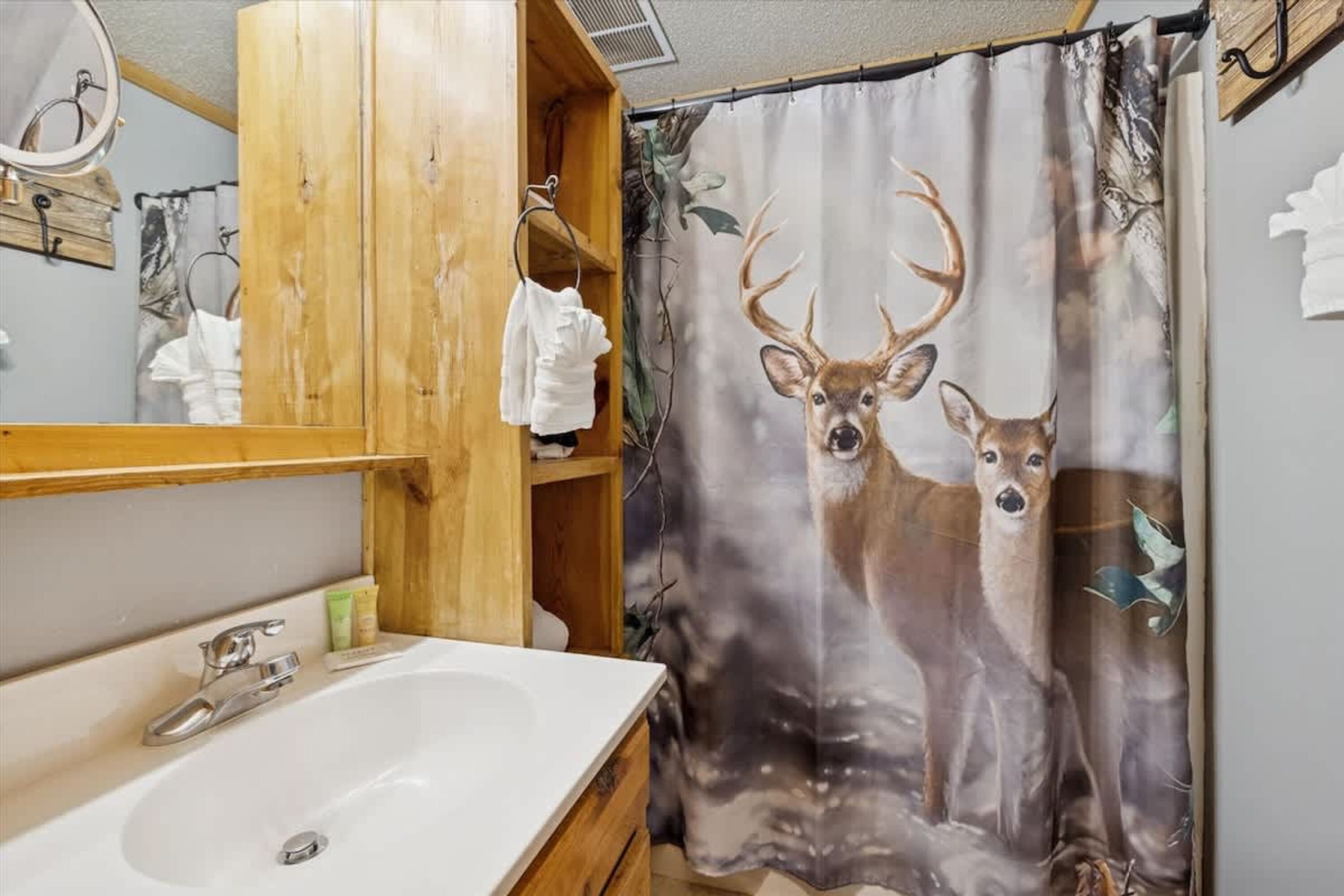 A bathroom with a wooden vanity, a sink, and a shower curtain with deer imagery.