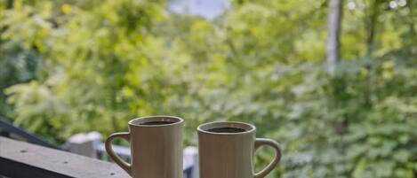 Two beige mugs on a wooden railing with a blurred green background.