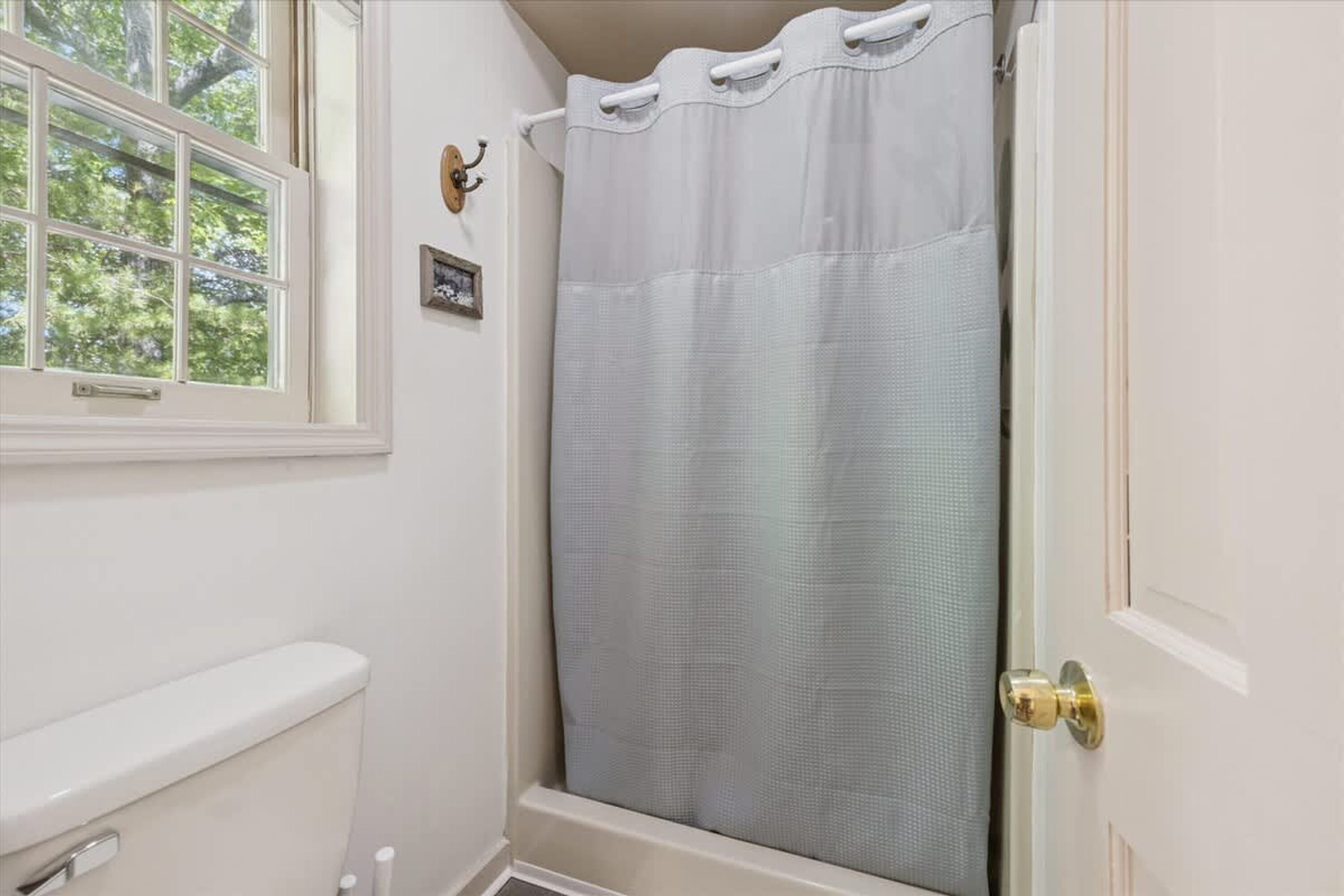 A bathroom with a white toilet, a shower curtain, and a window with a view of trees.